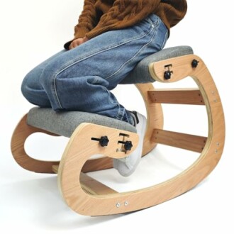Person sitting on an ergonomic kneeling chair with a wooden frame.
